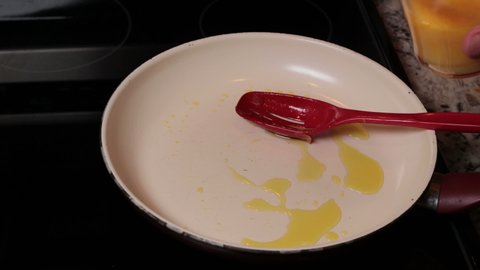 Organic egg yolks poured into a frying pan with oil and a hand stirring and cooking with a red spoon. Man pouring pasture raised uncooked eggs into a stovetop cooking pan and preparing breakfast.