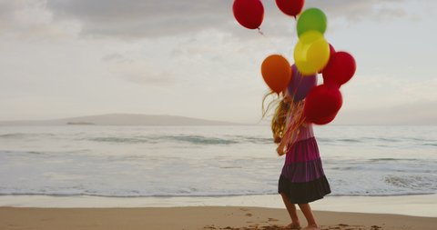 Happy young girl playing on the beach with balloons at sunset