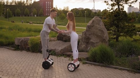 A young sports couple rides a gyro scooter and kissed in a beautiful Park in the summer at sunset. Happy man and woman riding on the hoverboard. Active lifestyle. Summer vacation.