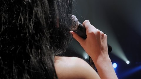 Portrait of a beautiful singer with long hair on a dark smoky stage in the spotlight. Female singer on the stage holding a microphone.