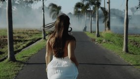 Video of a beautiful young European brunette girl running on the empty road with palm trees in the bali