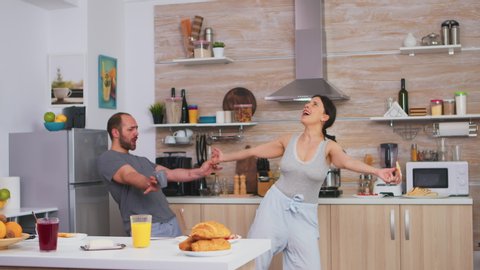 Cheerful couple dancing in kitchen and having fun during breakfast. Carefree husband and wife laughing, singing, dancing listening musing, living happy and worry free. Positive people