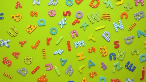 Colorful magnetic, plastic and paper alphabet letters placed randomly on green background. Top view, flat lay.