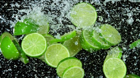 Super Slow Motion Shot of Flying Fresh Lime Slices and Water Side Splash Isolated on Black Background at 1000fps.