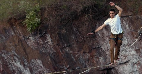 Extreme sport, a man is walking and balancing on the slackline over a quarry, 4k