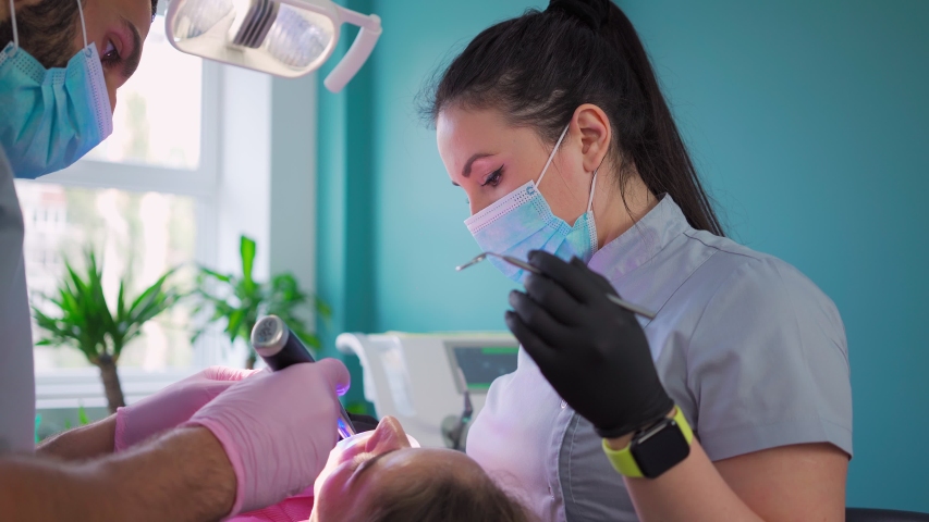 Two doctors, man and woman in protective masks in a dental clinic, serve the patient girl. Work Dentist. Healthcare and medicine concept. Steadicam shooting. Royalty-Free Stock Footage #1055304500