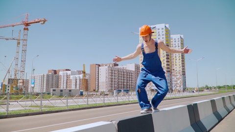 Happy Caucasian Man Builder in Hard Hat Dancing. Worker Funny Moves Against the Background of the Construction Site. Slow motion. Steadicam shooting.