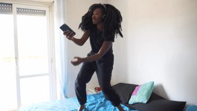 Slow motion shot of young woman dancing and using smartphone on bed