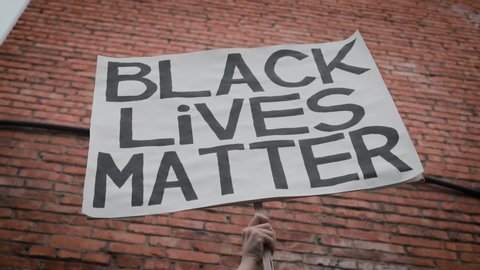 A Hand Holding up a Poster with the Slogan Black Lives Matter Against the background of a Brick Building. The Concept Of Stop Racism, No Racism.