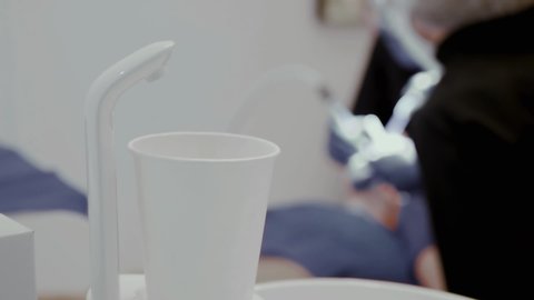 Dental faucet and paper cup on the background of an unrecognizable woman patient treats teeth with copy space. Dental health concept