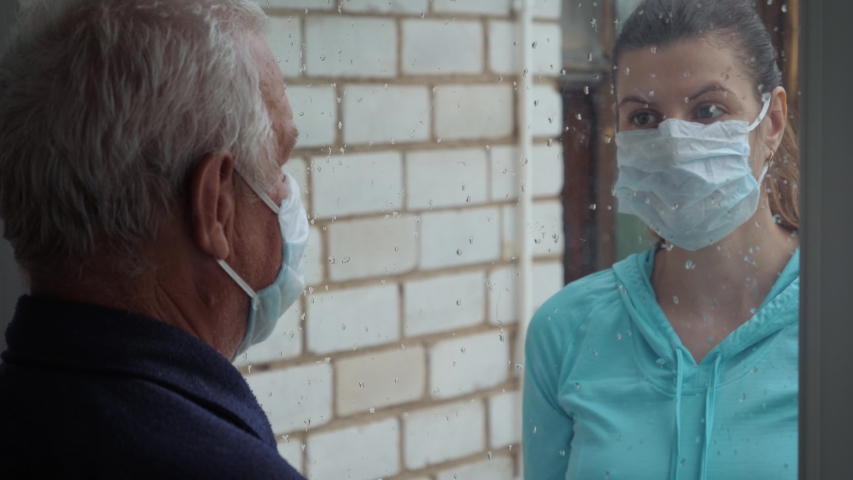 Woman in protective medical mask and illness old man touch their hands through glass window that separates them. Quarantine for coronavirus pandemic. Hope hand and support for recovery from covid-19 | Shutterstock HD Video #1055309036