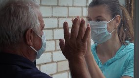Woman in protective medical mask and illness old man touch their hands through glass window that separates them. Quarantine for coronavirus pandemic. Hope hand and support for recovery from covid-19 - Powered by Shutterstock - Get 15% off with code: PIKWIZARD15