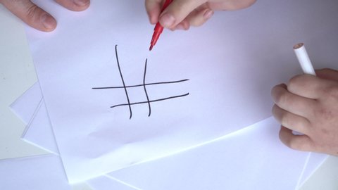 View of the hands of dad and a small child. Dad plays tic tac toe with his daughter on a sheet of paper.