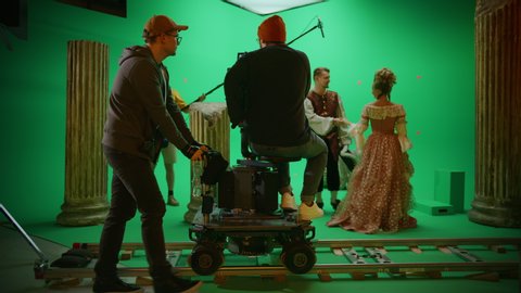 On Film Studio Set Shooting History Movie Green Screen Scene. Moving Cameraman on Railway Trolley Shooting Two Costumed Actors while Director Controls Process. Professional Crew on Big Budget Film