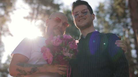 Portrait of Loving Male Gay Couple Meeting On Date Giving Partner Hug And Bunch Of Flowers