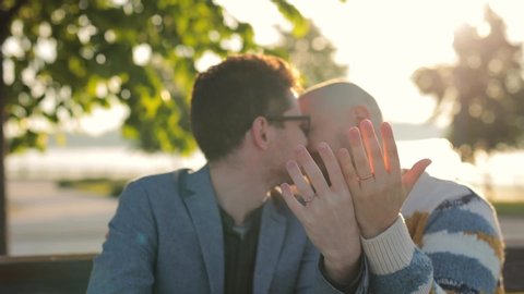 Gay Marriage Proposal Concept. Adorable Boyfriend kissing and show his Beautiful Shiny Wedding Rings to camera. Surprised Partner is Extremelly Happy and Hugs His Queer Friend. Relationship Goals.