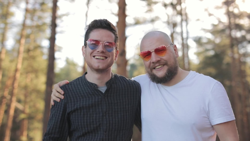 Gay Couple in heart sunglasses stay at park and show in camera red heart simbol