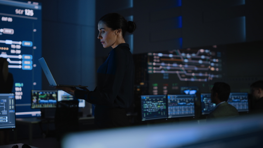 Beautiful Confident Female Project Leader works on a Laptop Standing in Telecommunications System Control Room. In Background Big Screen Showing Infographics of Infrastructure, Charts, System Analysis Royalty-Free Stock Footage #1055317502