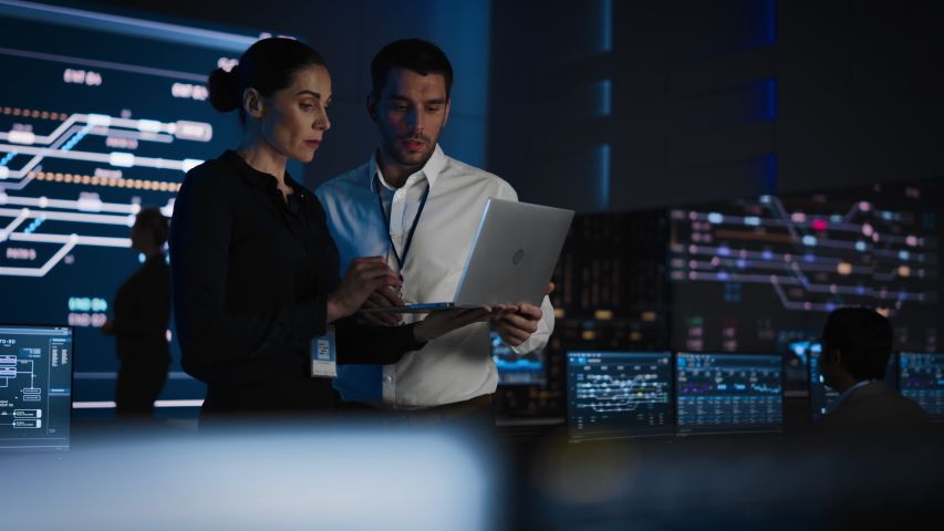 Project Leader and Chief Executive Discuss Data Shown on a Laptop. In Background Big Screen Showing Infographics of Infrastructure, Charts, System Analysis.Telecommunications Control Room - Powered by Shutterstock - Get 15% off with code: PIKWIZARD15