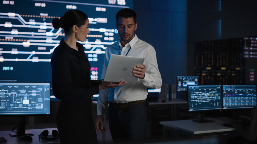 Project Leader and Chief Executive Discuss Data Shown on a Laptop. In Background Big Screen Showing Infographics of Infrastructure, Charts, System Analysis.Telecommunications Control Room - Powered by Shutterstock - Get 15% off with code: PIKWIZARD15