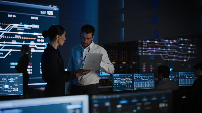 Project Leader and Chief Executive Discuss Data Shown on a Laptop. In Background Big Screen Showing Infographics of Infrastructure, Charts, System Analysis.Telecommunications Control Room - Powered by Shutterstock - Get 15% off with code: PIKWIZARD15