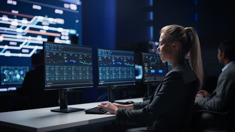 Confident Female Data Scientist Works on Personal Computer in Big Infrastructure Control Room. Stock Market Woman Specialist Uses Computer Showing Graphs, Charts, Information. Monitoring Room Team