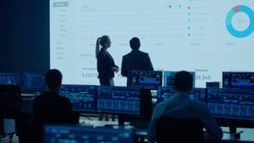 Project Leader and Chief Executive Discuss Data Shown on Big Display. Screens Show Infographics, Charts, Finance Analysis, Stock Market, Growth.Telecommunications Control Room Working Professionals - Powered by Shutterstock - Get 15% off with code: PIKWIZARD15