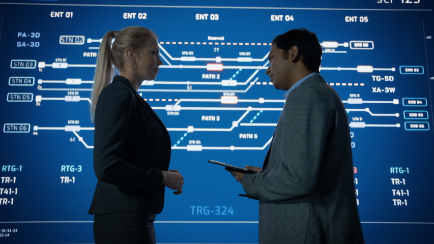 Project Manager and Computer Science Engineer Talking while Using Big Screen Display Showing Infrastructure Infographics, Data. Telecommunications Company System Control and Monitoring Room. Zoom out Royalty-Free Stock Footage #1055317613