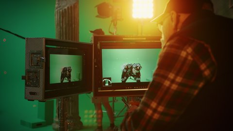 Director Looks at Displays Directs Green Screen CGI Scene with Actor Wearing Motion Tracking Suit and Head Rig. In the Big Film Studio Professional Crew Shooting Blockbuster Movie