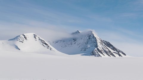 Timelapse of clouds and fog covering a white snowy mountain peak in a glacier area at Antarctica, South Pole