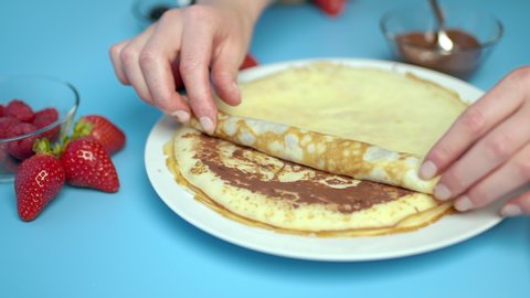 Adding/putting chocolate on french crepes in a serving plate. Concept of preparing french crepes/pancakes at home.