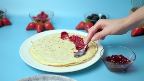 Adding/putting Roseberry jam on french crepes in a serving plate. Concept of preparing french crepes/pancakes at home.
