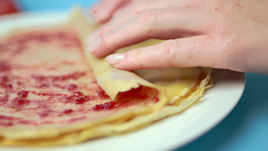 Adding/putting Roseberry jam on french crepes in a serving plate. Concept of preparing french crepes/pancakes at home. Royalty-Free Stock Footage #1055320475