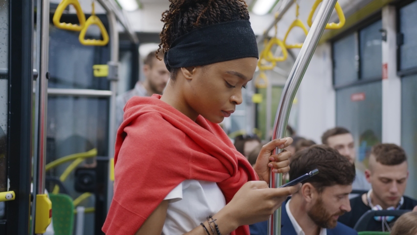 Young afro-american black girl using mobile phone internet social network application while traveling by bus to city center. Citizens. Diverse people. Public transport. Royalty-Free Stock Footage #1055325122