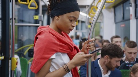 Young afro-american black girl using mobile phone internet social network application while traveling by bus to city center. Citizens. Diverse people. Public transport.