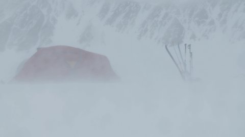 A tent is struggeling and almost gets blown away during a heavy snowstorm in cold and icy winter conditions