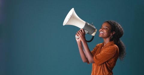 Portrait of beautiful young black woman with curly hair, shouting through a megaphone on blue background
