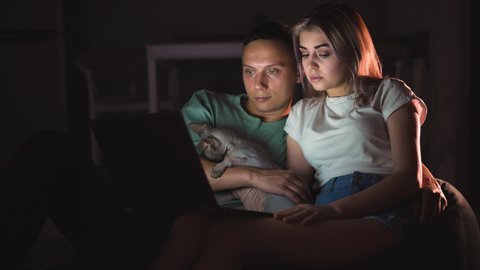 young couple guy and girl are sitting at home in the evening and watching a movie online. Sphynx hairless cat in the arms.
