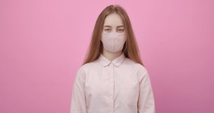 Portrait of charming girl with blond hair wearing pink medical mask and shirt posing in studio with pink background. Concept of health care and protection from coronavirus.