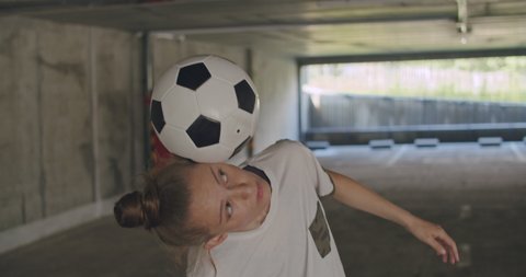 Teenager girl football soccer player practicing tricks, kicks and moves with ball inside empty covered parking garage. Urban city lifestyle outdoors concepte. 4K UHD slow motion RAW graded footage