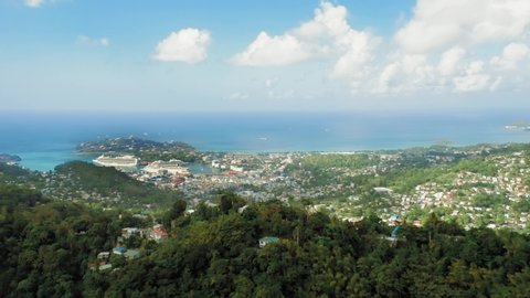 Aerial shot of the horizon where the sky merges with the sea. On the shore of the mountain, a dense forest and a city with vessels.(Rodney Bay, Saint Lucia)