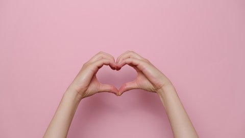 Close up of beautiful female hands making heart symbol, isolated on pink studio background with copy space for advertisement. Love and body language concept