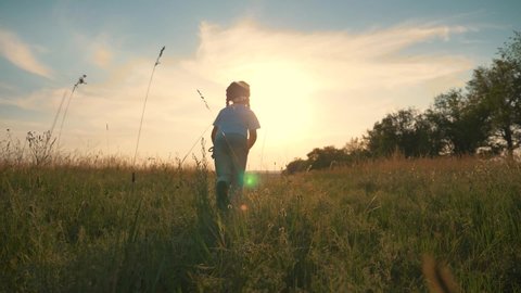 A healthy, happy, carefree child runs along a green summer field, enjoying nature, fresh air, moving towards goal, dream. happy family. A girl at sunset on a summer day.