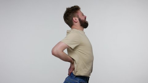 Bearded man suffering backache, massaging sore place lower spine, frowning from unbearable spasm torn muscles and tendons, kidney stones, pinched nerve. indoor studio shot isolated on gray background