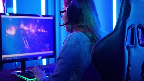 Esports gamer woman playing game online on PC computer at home. Asian girls controlling mouse and keyboard competition in video game. Teenage girls leisure game in cyberpunk neon light room at home.
