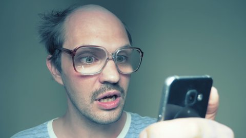 a balding man with glasses uses a smartphone. gesture surprise victory. Humor.