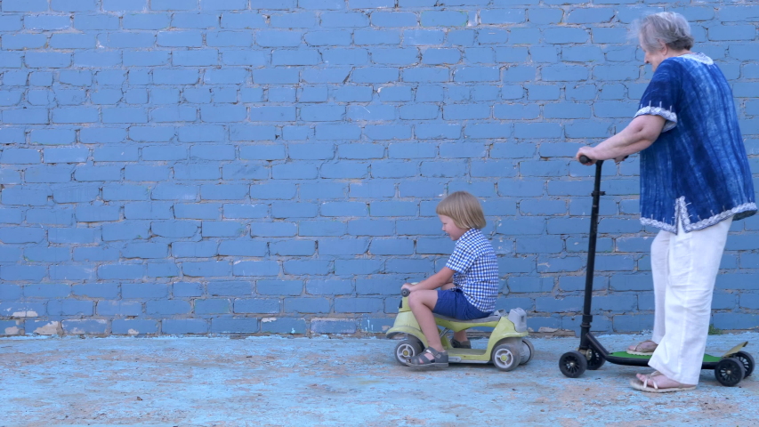Funny blond boy in plaid shirt riding bicycle with his beloved grandmother. child teaches an elderly granny to ride. pensioner is smartly dressed and rolls on a large stretched scooter