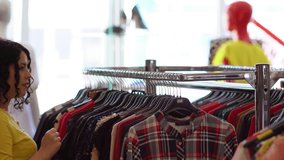 Young woman looking at a checked top hanging on a rail in a clothing shop before passing on to a black lacy blouse further along