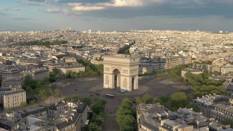 France, Paris Arc de Triomphe (Triumphal Arch) in Champs Elysees, with Sacré-Coeur Basilica church in the background at sunset (or sunrise). 4k quality drone shot, aerial view from right to left