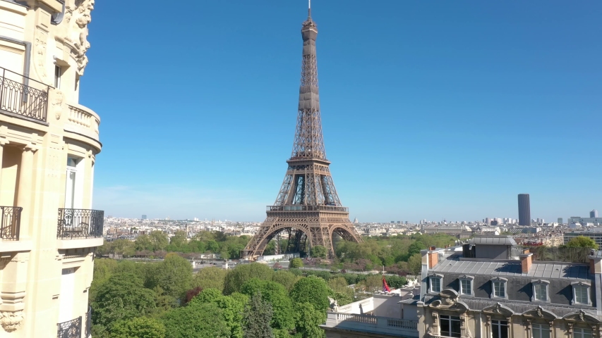 France, Paris Tour Eiffel (Eiffel tower) with blue sky and green trees in the foreground. 4k quality drone shot, aerial view from bottom to top (looks like crane shot)